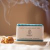 Throat Chakra Soap, wrapped on stone soap dish and cream linen with blurred smoking incense cone and flower buds | Shine Body & Bath