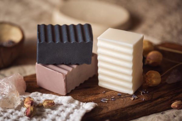 Group of three higher Chakra soaps | Crown Chakra Soap, Third Eye Chakra Soap, Throat Chakra Soap on wooden board with scattered lavender petals, flower buds, and crystals | Shine Body & Bath