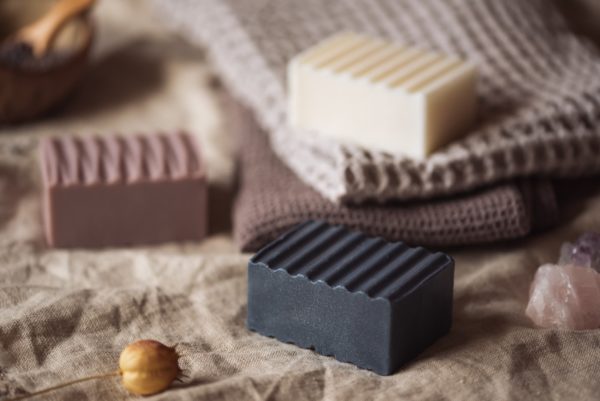Group of three higher Chakra soaps | Crown Chakra Soap, Third Eye Chakra Soap, Throat Chakra Soap on Cream and lavender coloured towwls and linen with scattered flower buds, and crystals | Shine Body & Bath