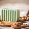 Heart Chakra Soap, unwrapped on cork board and cream waffle fabric with dried ear of grass and bowl of rose buds, blurred background | Shine Body & Bath