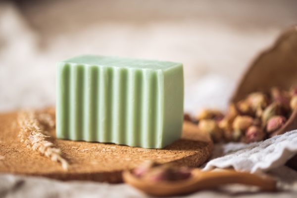Heart Chakra Soap, unwrapped on cork board and cream waffle fabric with dried ear of grass and bowl of rose buds, blurred background | Shine Body & Bath