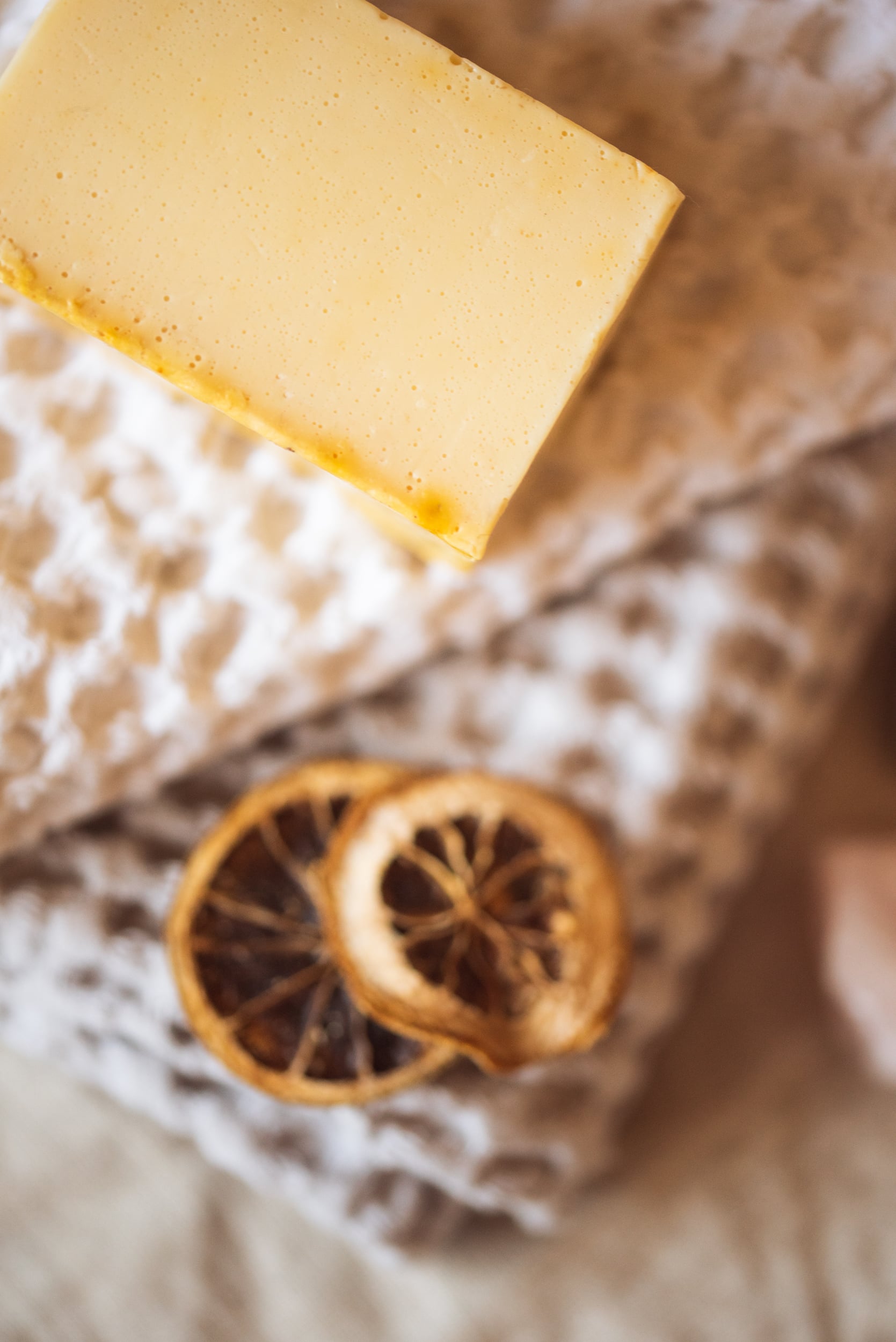 Close up of corner of Solar Plexus Chakra Soap, unwrapped on cream waffle fabric with two dried lemon slices | Shine Body & Bath