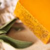 Up close corner of Sacral Chakra Soap, unwrapped on cream linen with sprig of green herbs | Shine Body & Bath