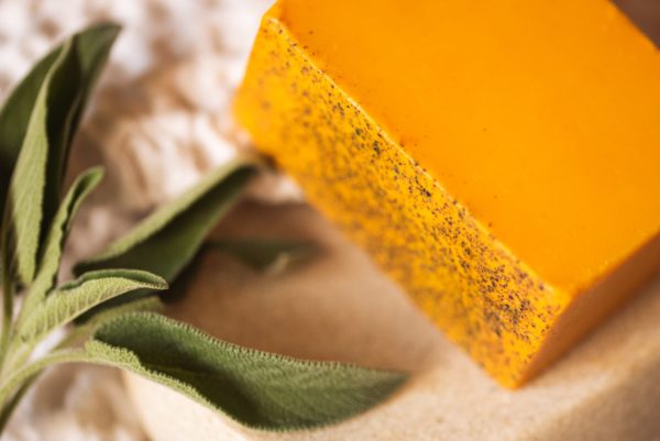 Up close corner of Sacral Chakra Soap, unwrapped on cream linen with sprig of green herbs | Shine Body & Bath