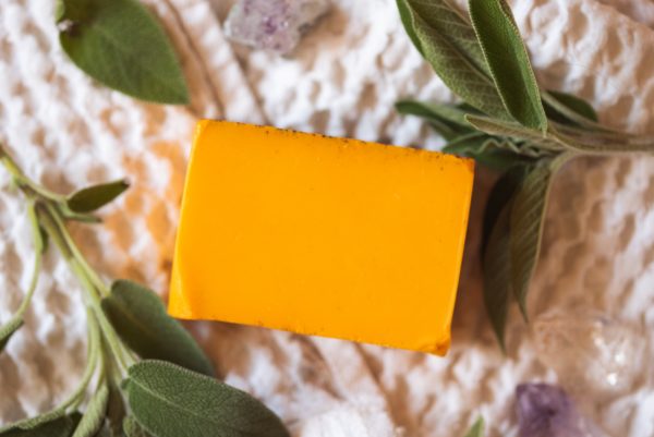 Sacral Chakra Soap, unwrapped on cream waffle fabric with scattered sprigs of green herbs and amethyst crystals | Shine Body & Bath