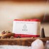 Root Chakra Soap, wrapped on wooden board with smoking incense cone, scattered dried petals and crystals | Shine Body & Bath