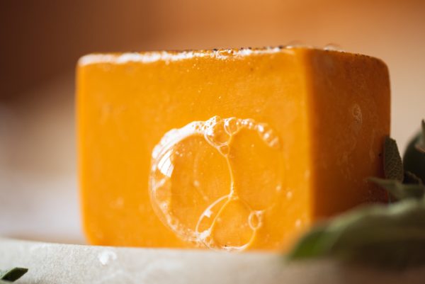 Sacral Chakra Soap, with bubbles sitting on a stone soap dish with herb leaves | Shine Body & Bath