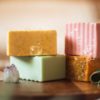 Group of lower chakra soaps - Root Chakra Soap, Sacral Chakra Soap, Solar Plexus Chakra Soap and Heart Chakra Soap, with bubbles, sitting on a wooden board with herbs and crystals | Shine Body & Bath