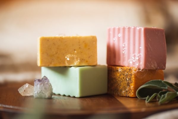 Group of lower chakra soaps - Root Chakra Soap, Sacral Chakra Soap, Solar Plexus Chakra Soap and Heart Chakra Soap, with bubbles, sitting on a wooden board with herbs and crystals | Shine Body & Bath