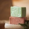 Group of two chakra soaps - Root Chakra Soap and Heart Chakra Soap, with bubbles, sitting on a stone soap dish with herbs | Shine Body & Bath