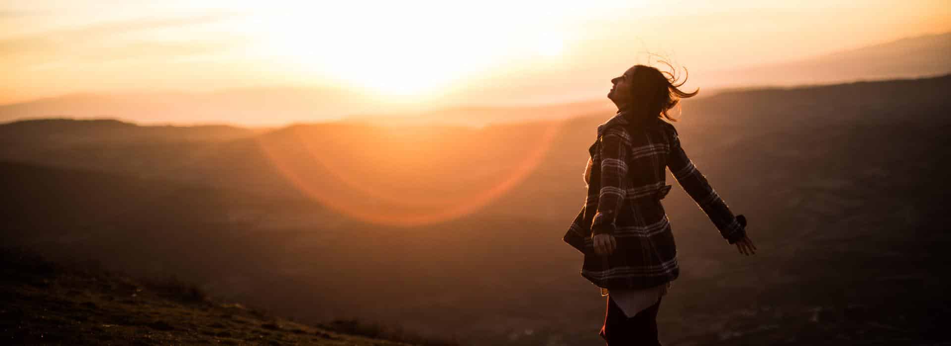 Essential Oils for Chakra Healing: Simple Scents to Balance Your Energy Blog | Woman standing in the wilderness in front of a sunset
