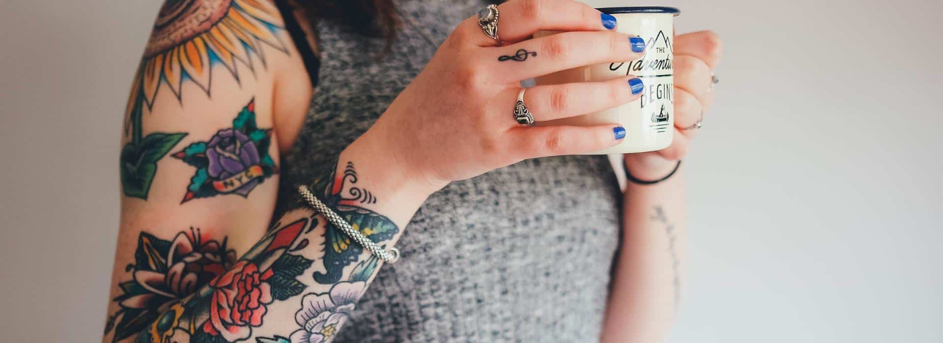 Sacred Skin: Why a Tattoo Balm is Essential for Your Ink (and Your Soul) | Image of Woman with tattoos holding a coffee cup